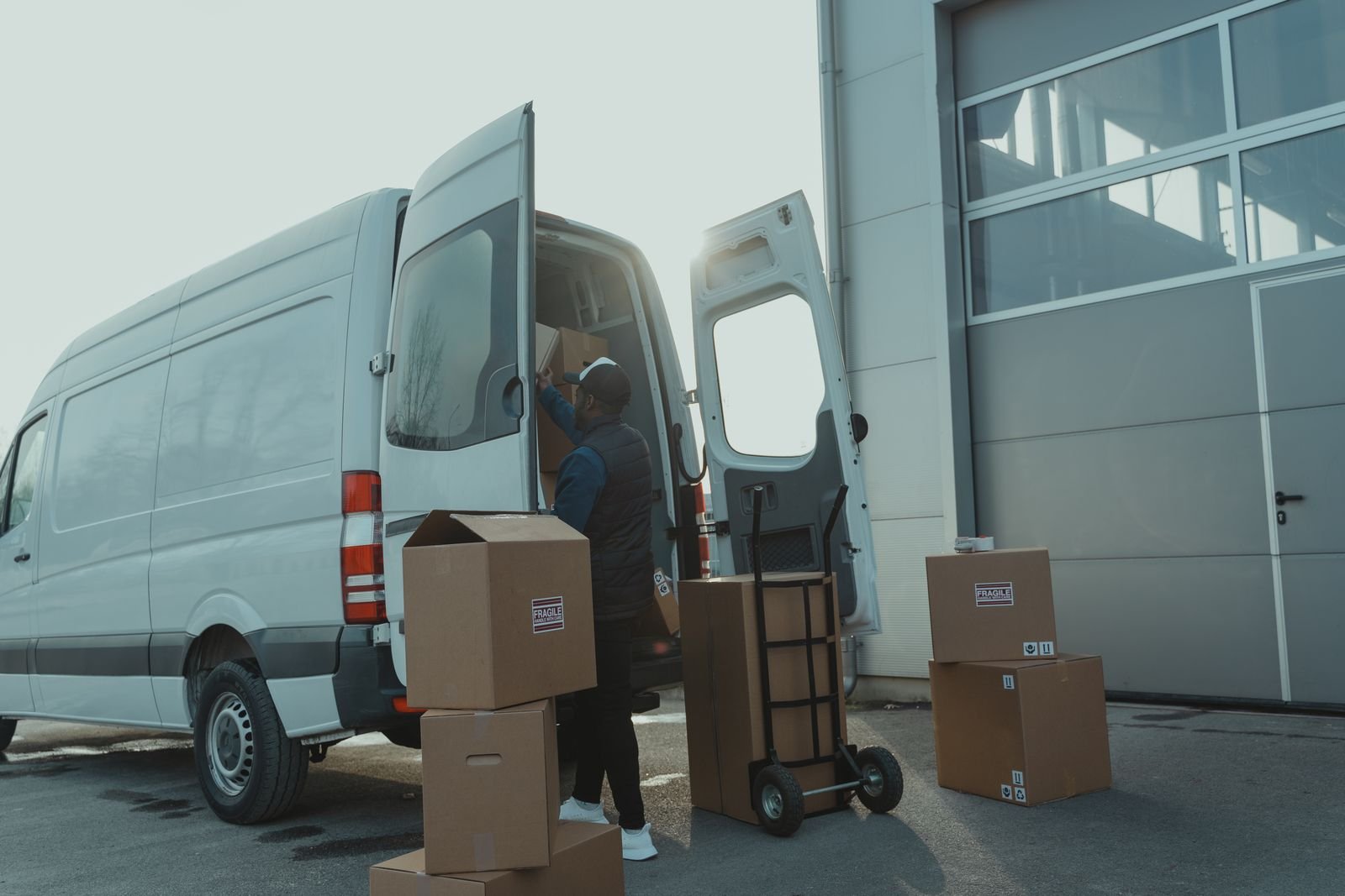 Courier loading packages into a white van in front of a warehouse