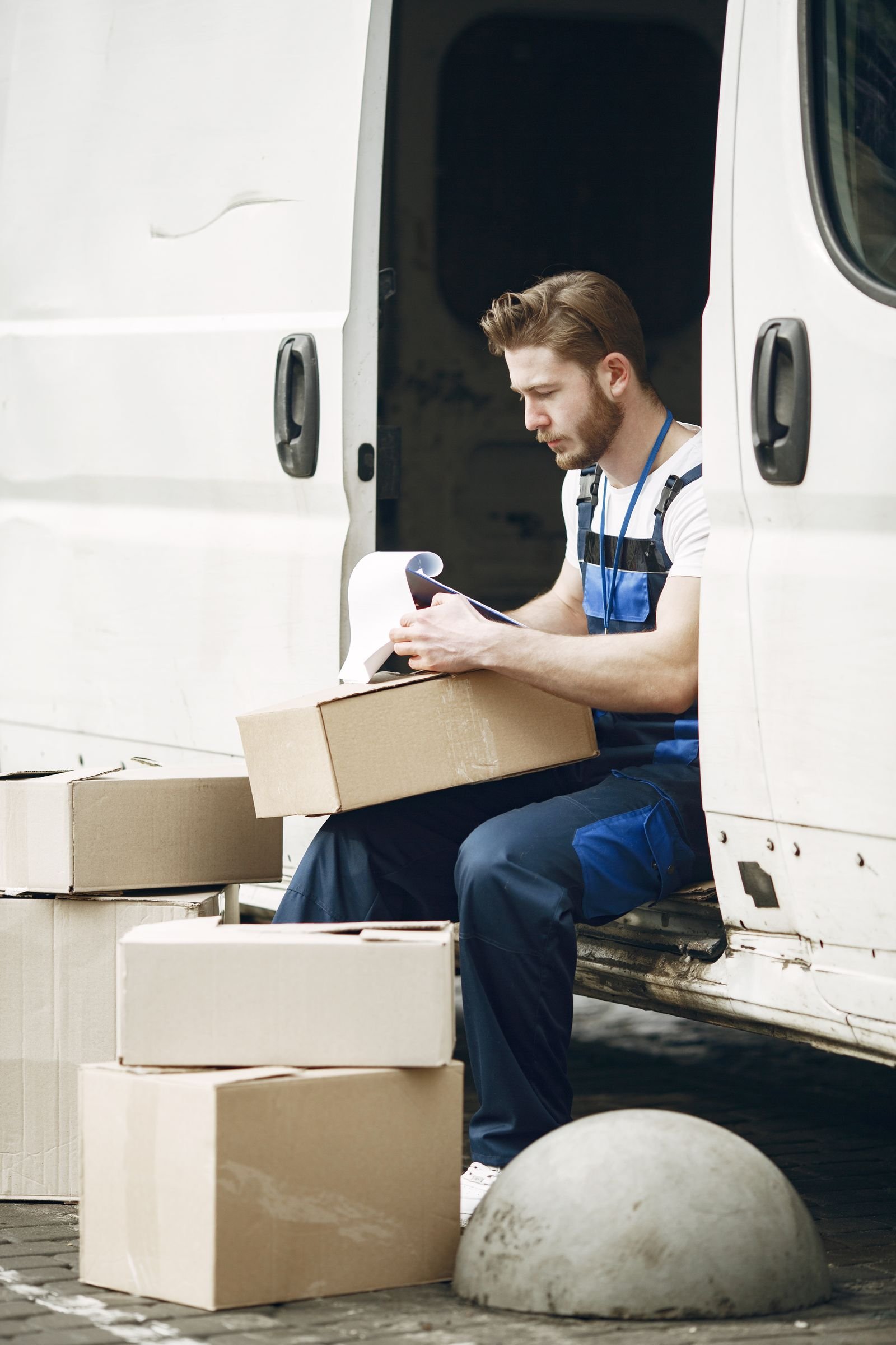 Courier in a blue uniform checking his route list next to the van